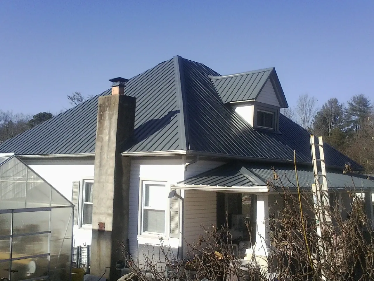 Dark blue standing seam metal roof on a white farmhouse with dormer — Slate & Tile Roof Repair by Roofing Brothers in East Spencer