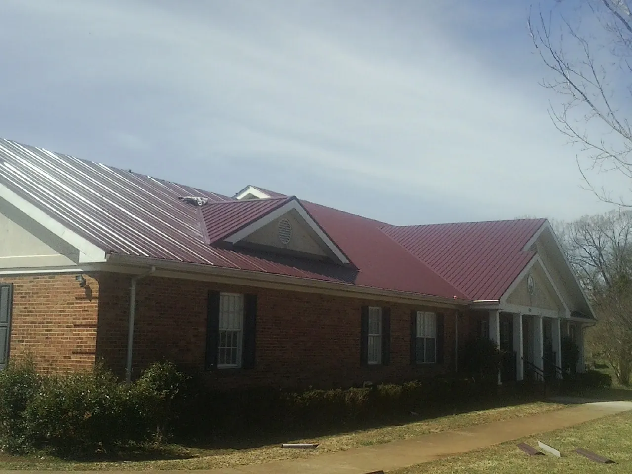 Red metal roof with gabled entries on a long brick building, from a Hail Damage Roof Repair job in East Spencer