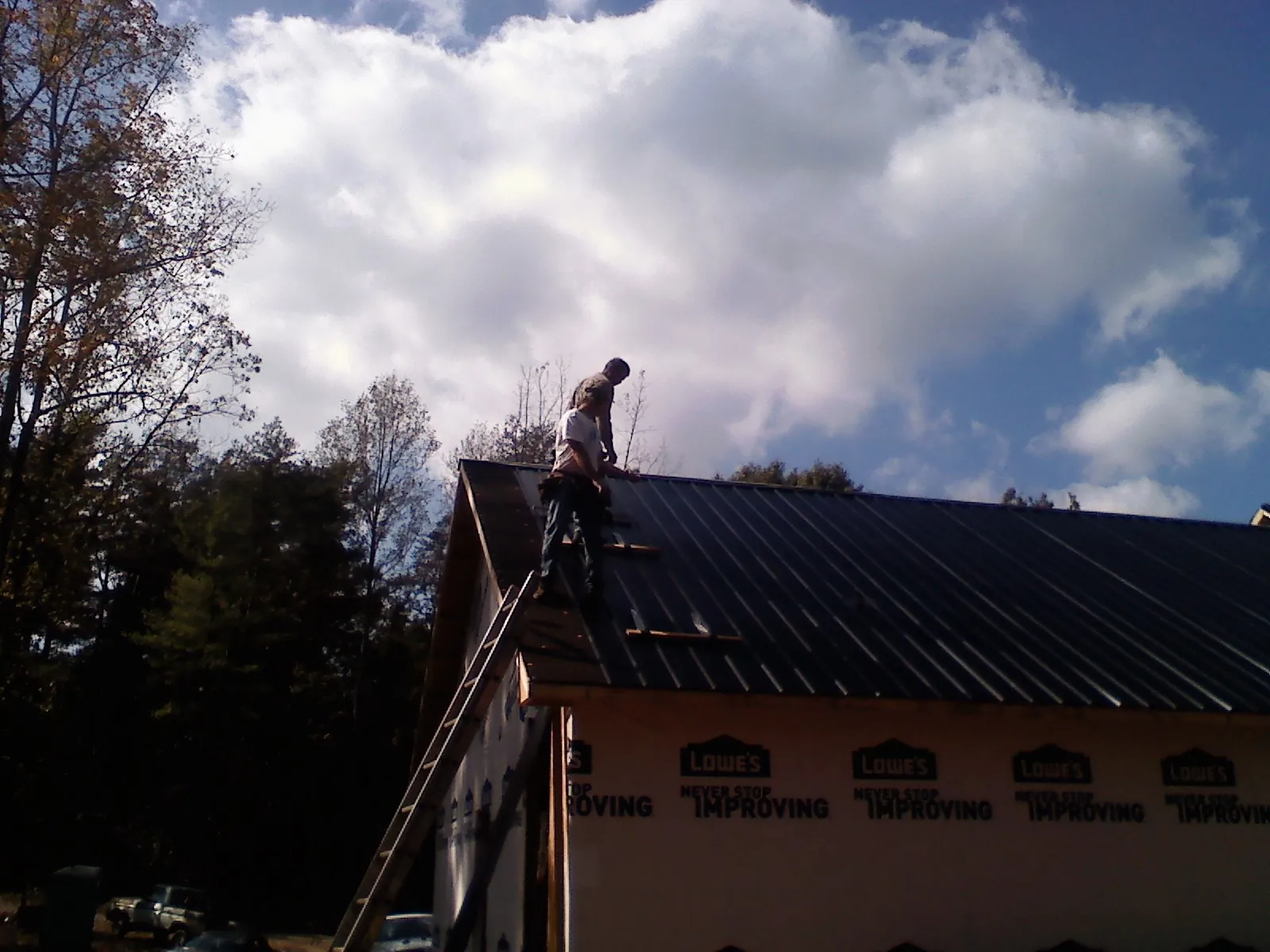 Roofer fastening dark metal panels high against a cloudy sky, from a Roof Inspection job in East Spencer