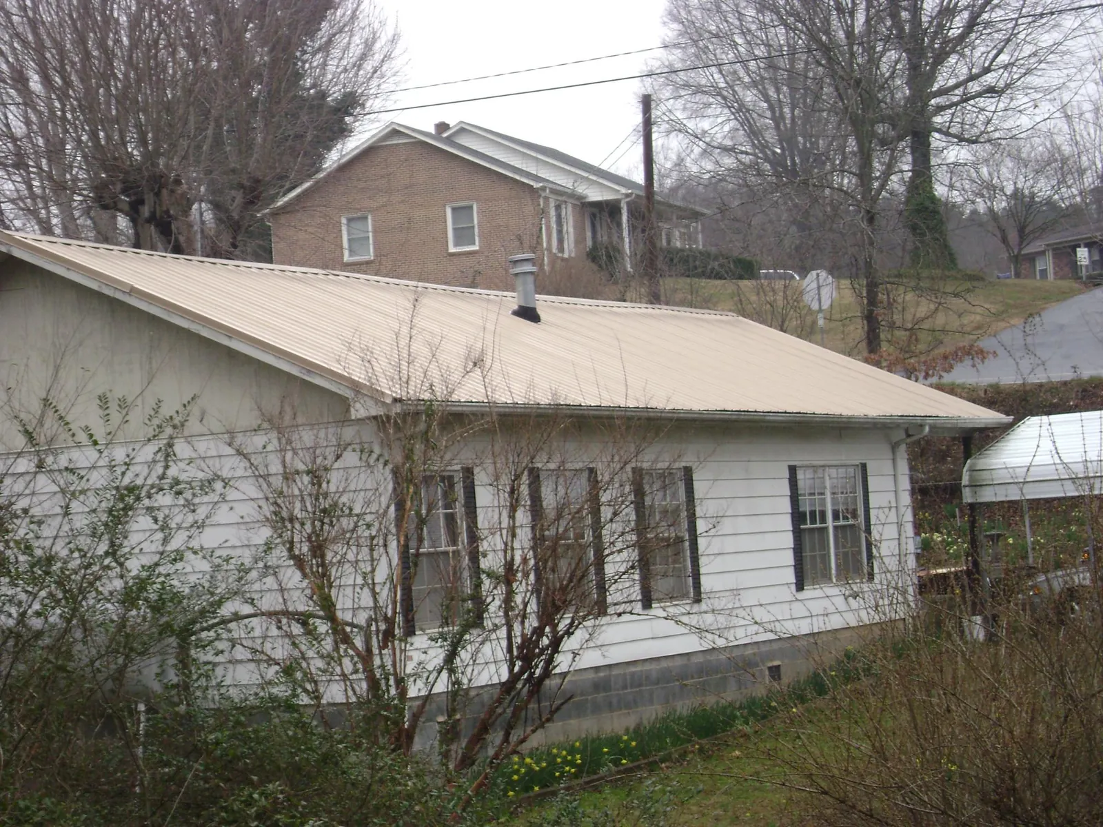 Tan metal roof on a white sided house set into a hillside — Commercial Roofing by Roofing Brothers in East Spencer