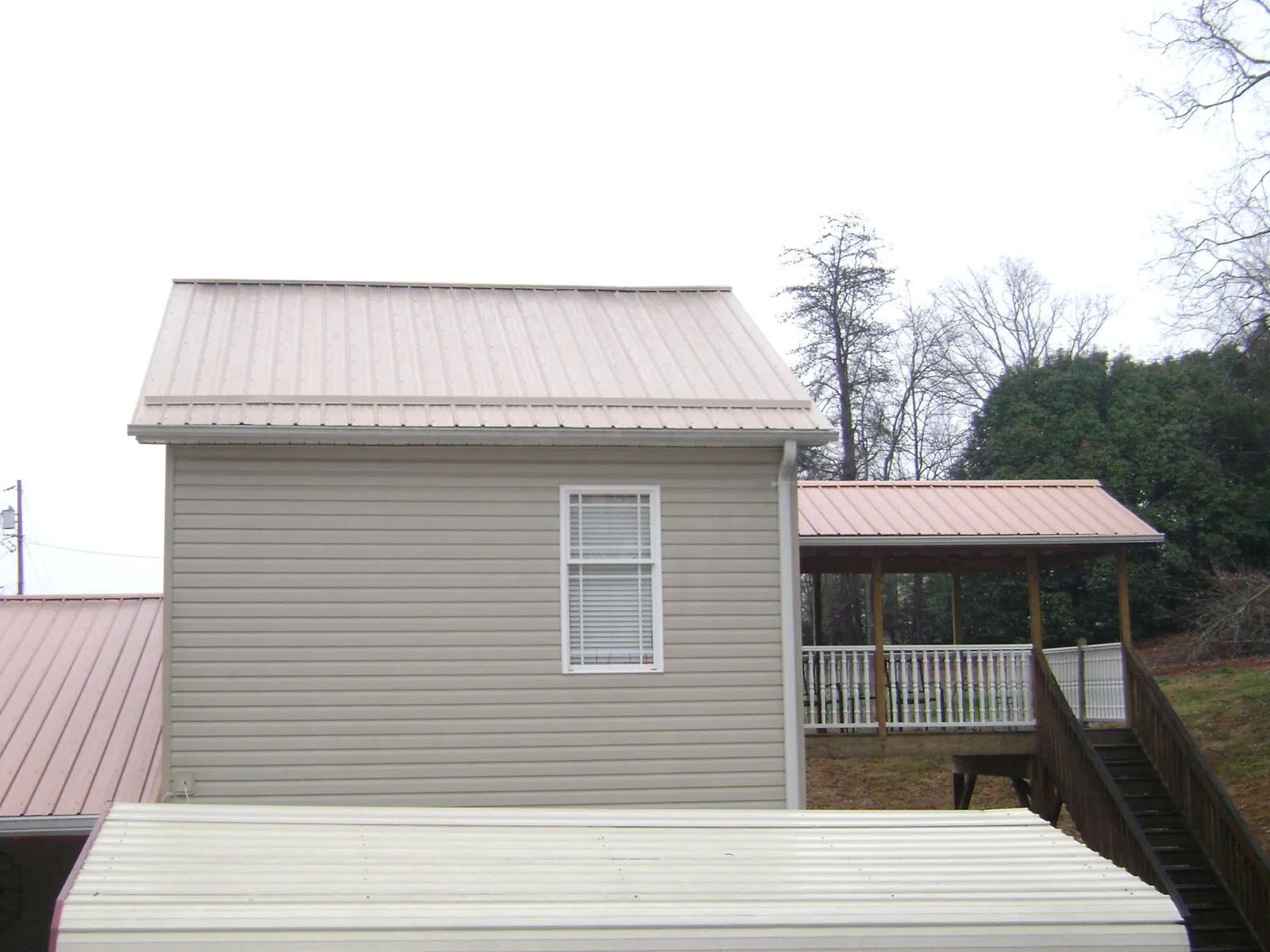Tan metal roofs on a two story addition and attached porch, from a Roof Replacement job in East Spencer